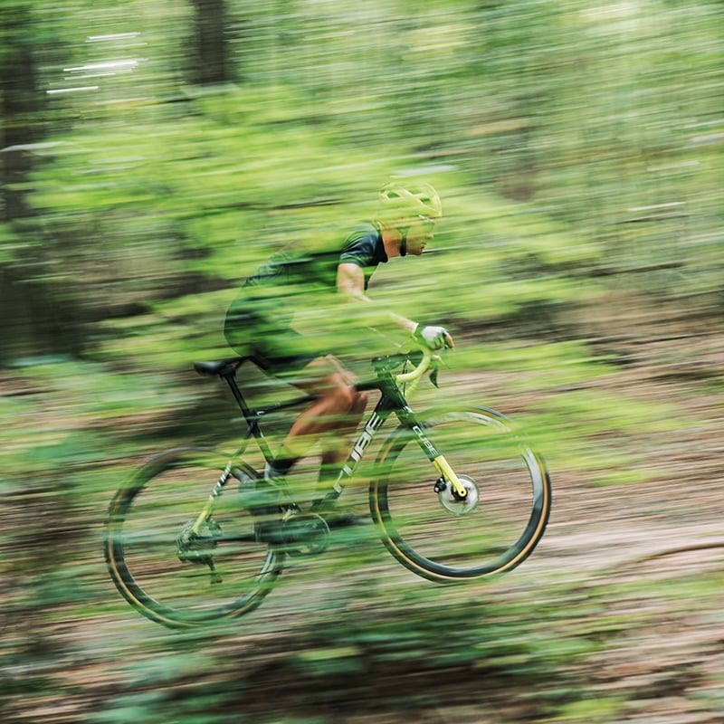 Radfahrer auf Cube Cross Race Fahrrad fährt schnell durch bewaldetes Gelände. Ideal für Geländefahrten und sportliche Radfahrer.