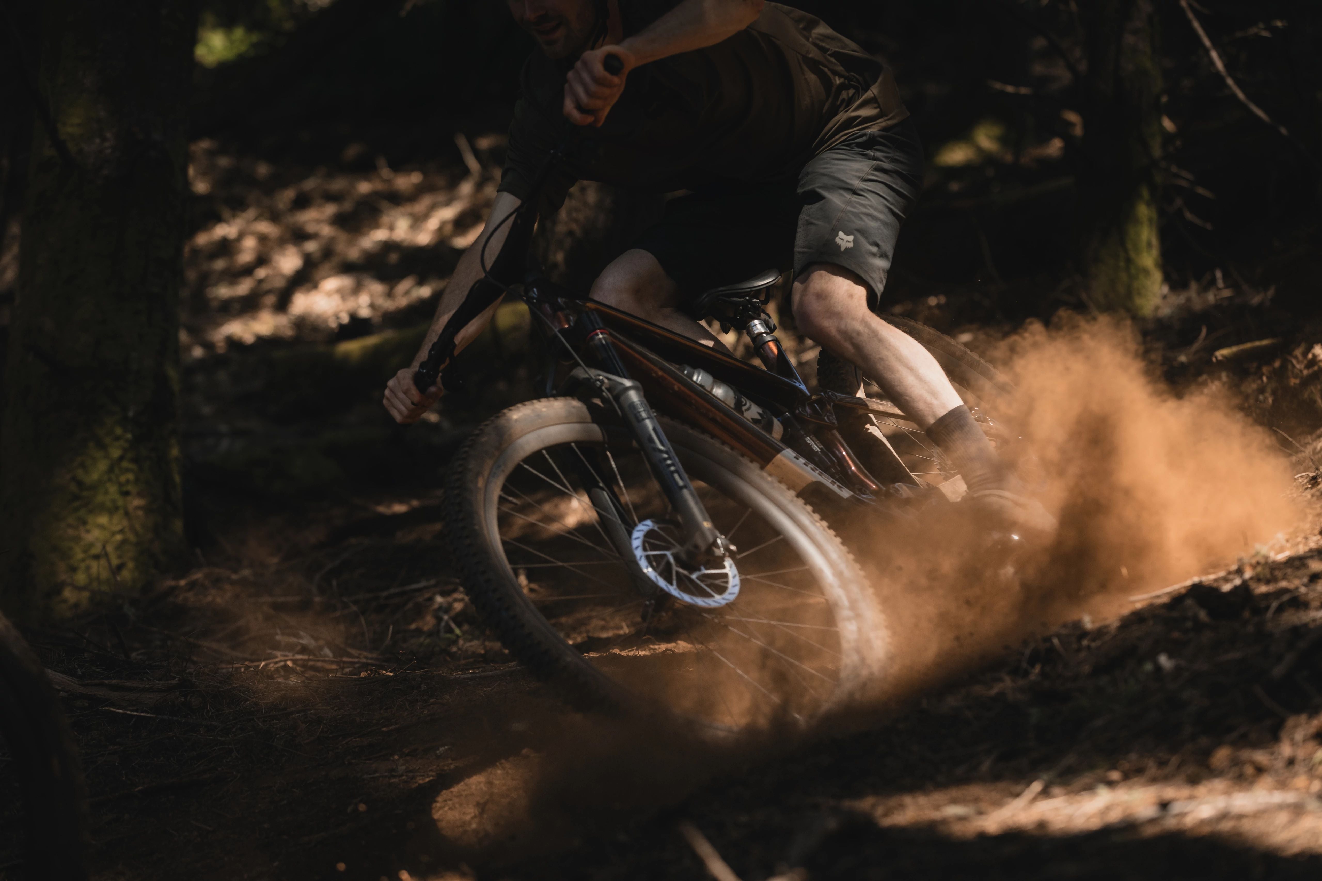 Mountainbiker in Aktion, wirbelt Staub auf, fährt Trek-Bike im Wald, ideal für Offroad-Abenteuer und Trail-Fans.