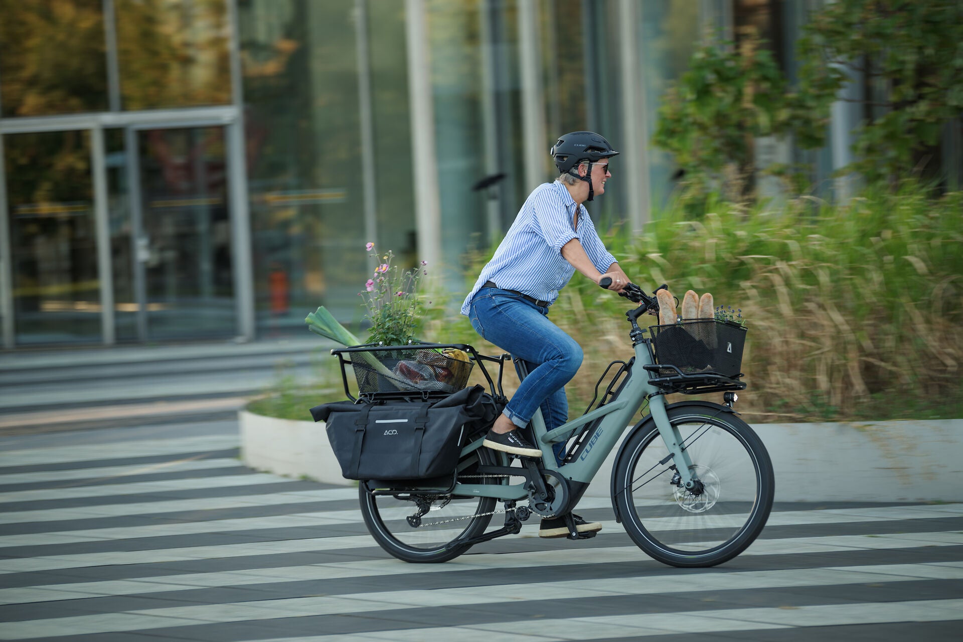 Person fährt ein Cube Longtail Hybrid-E-Bike mit Gepäckträger und Fahrradkorb, ideal für den urbanen Transport.