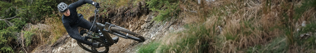 Mountainbiker mit Helm fährt ein schwarzes Fahrrad auf einem schmalen Waldpfad. Geeignet für Offroad-Enthusiasten.
