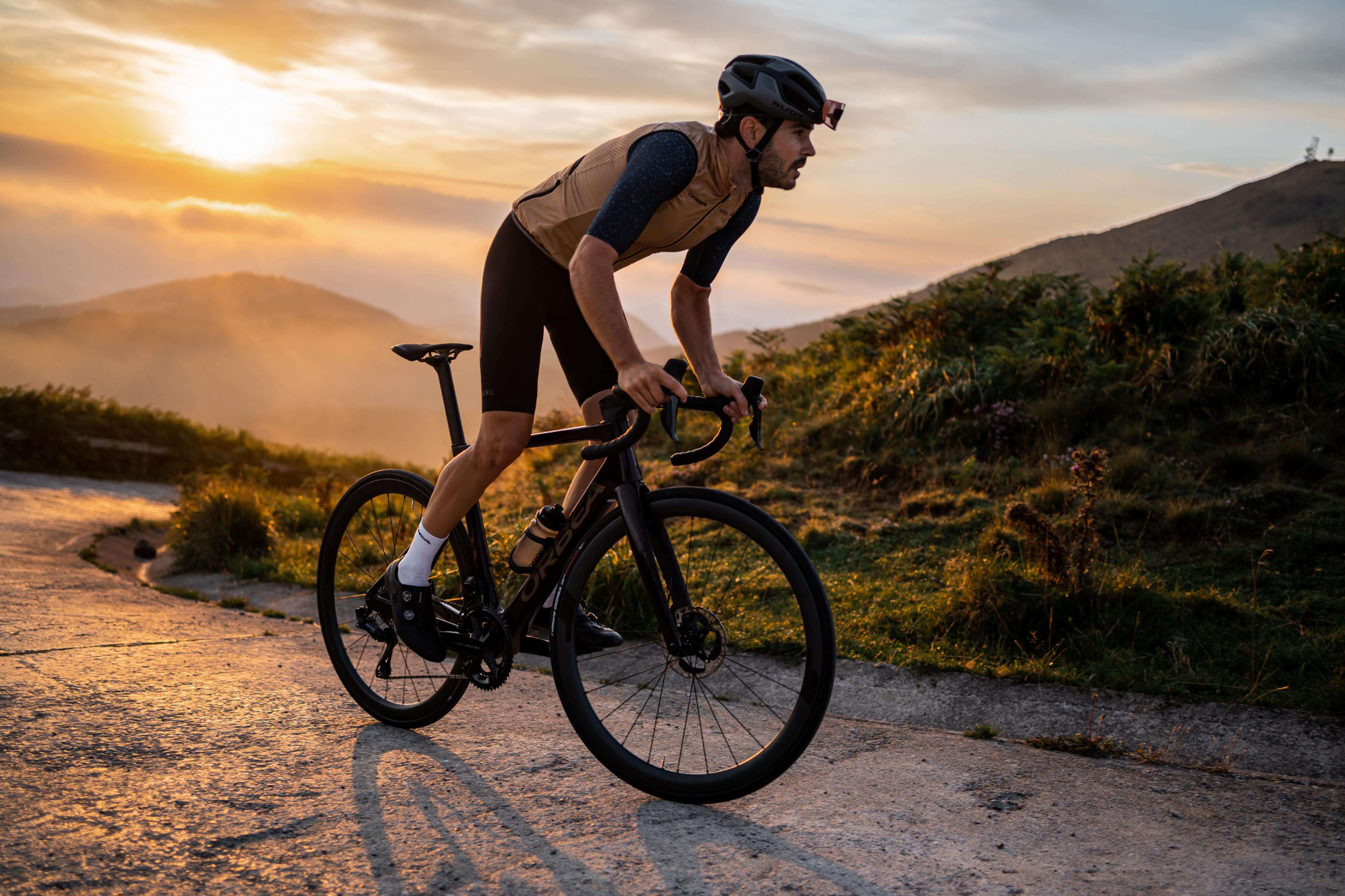 Radfahrer auf einem Orbea-Rennrad bei Sonnenuntergang auf einer ländlichen Straße.