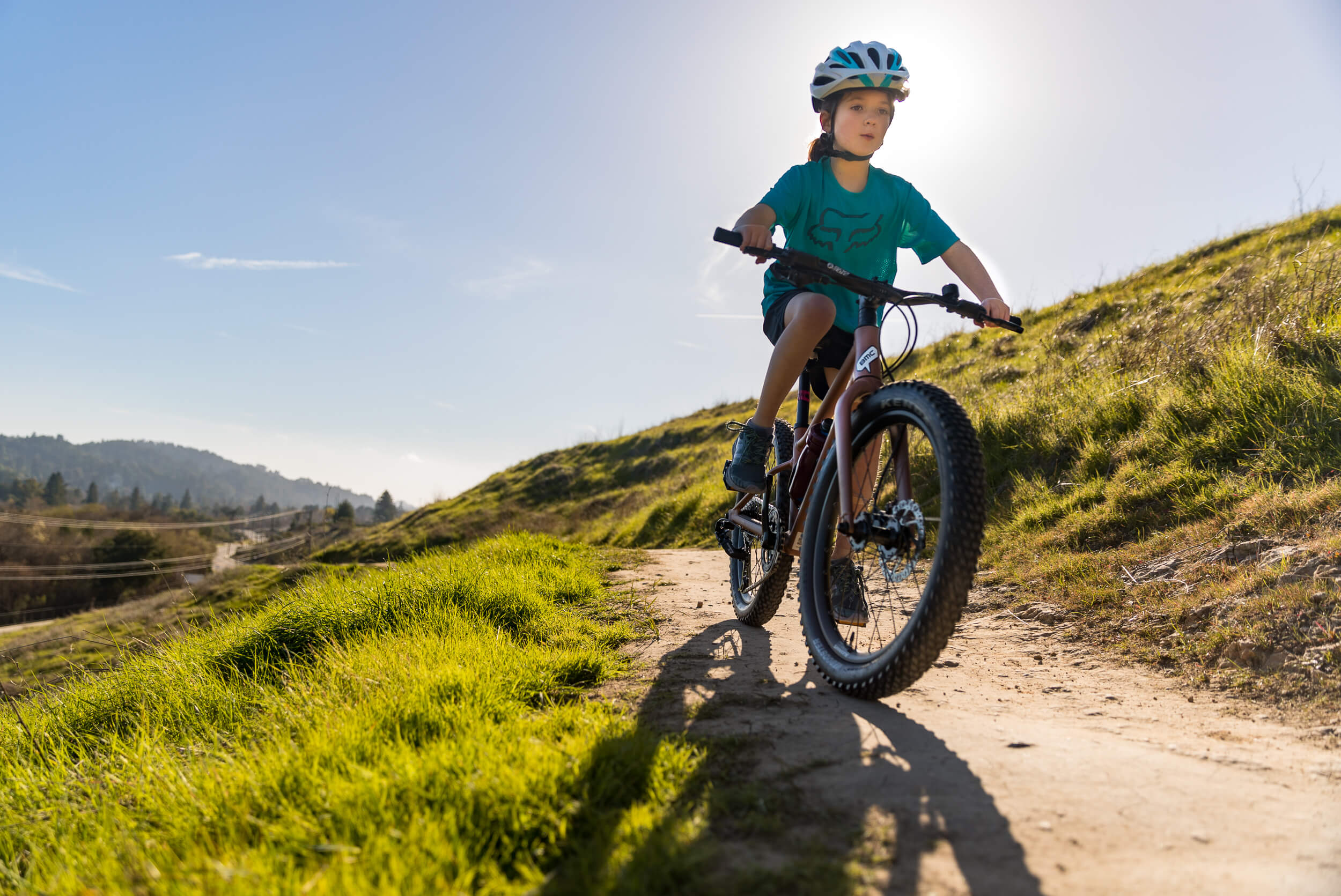 Kind mit Helm fährt auf einem Kinder-Mountainbike durch hügelige Landschaft.