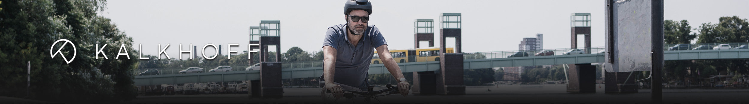 Mann auf Kalkhoff E-Bike mit Helm vor Brücke, urbaner Hintergrund, geeignet für Stadtfahrten.