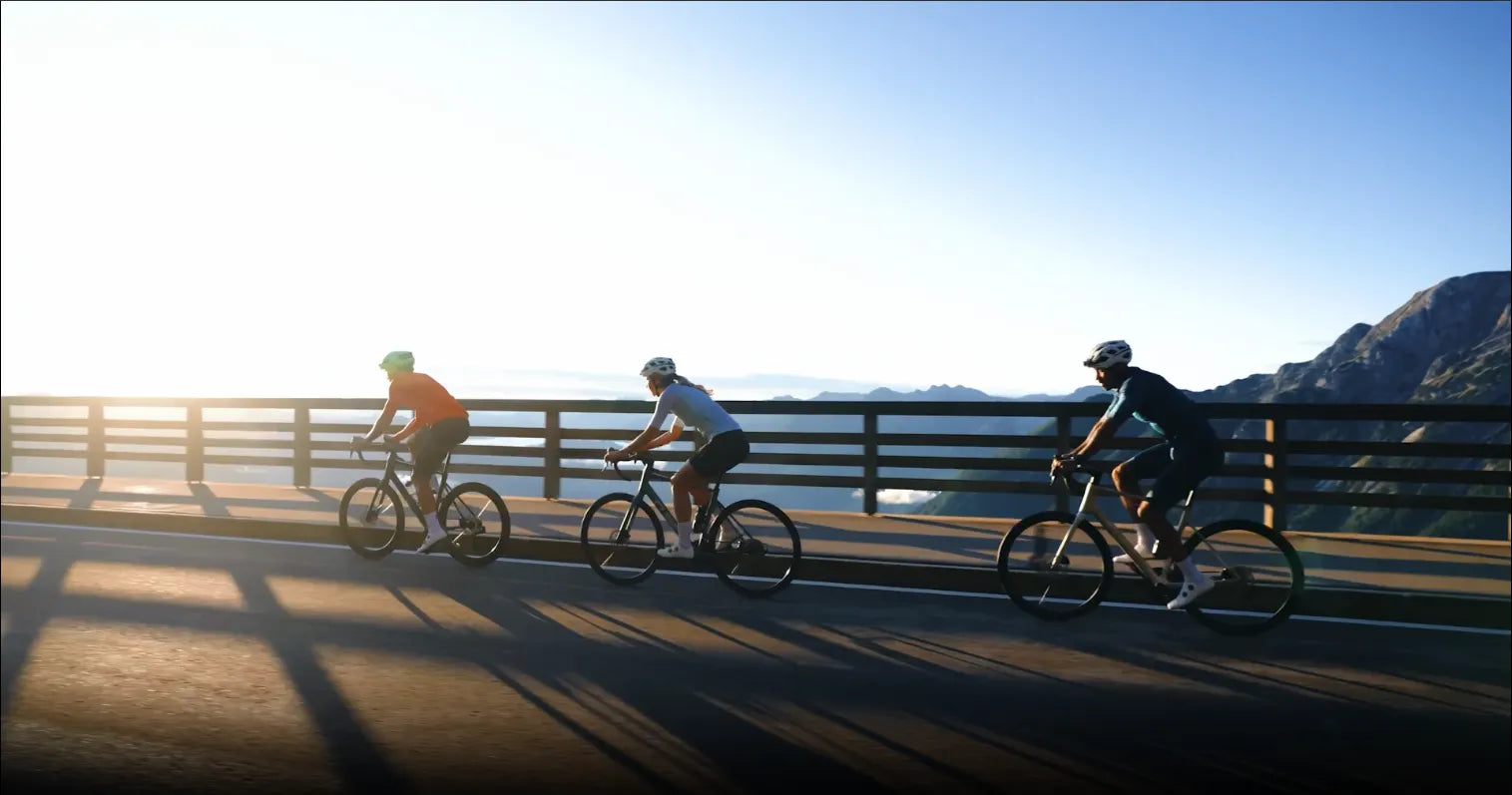 Drei Cube Attain Pro Radfahrer in Sportbekleidung fahren bei Sonnenaufgang über eine Brücke, umgeben von Bergen.