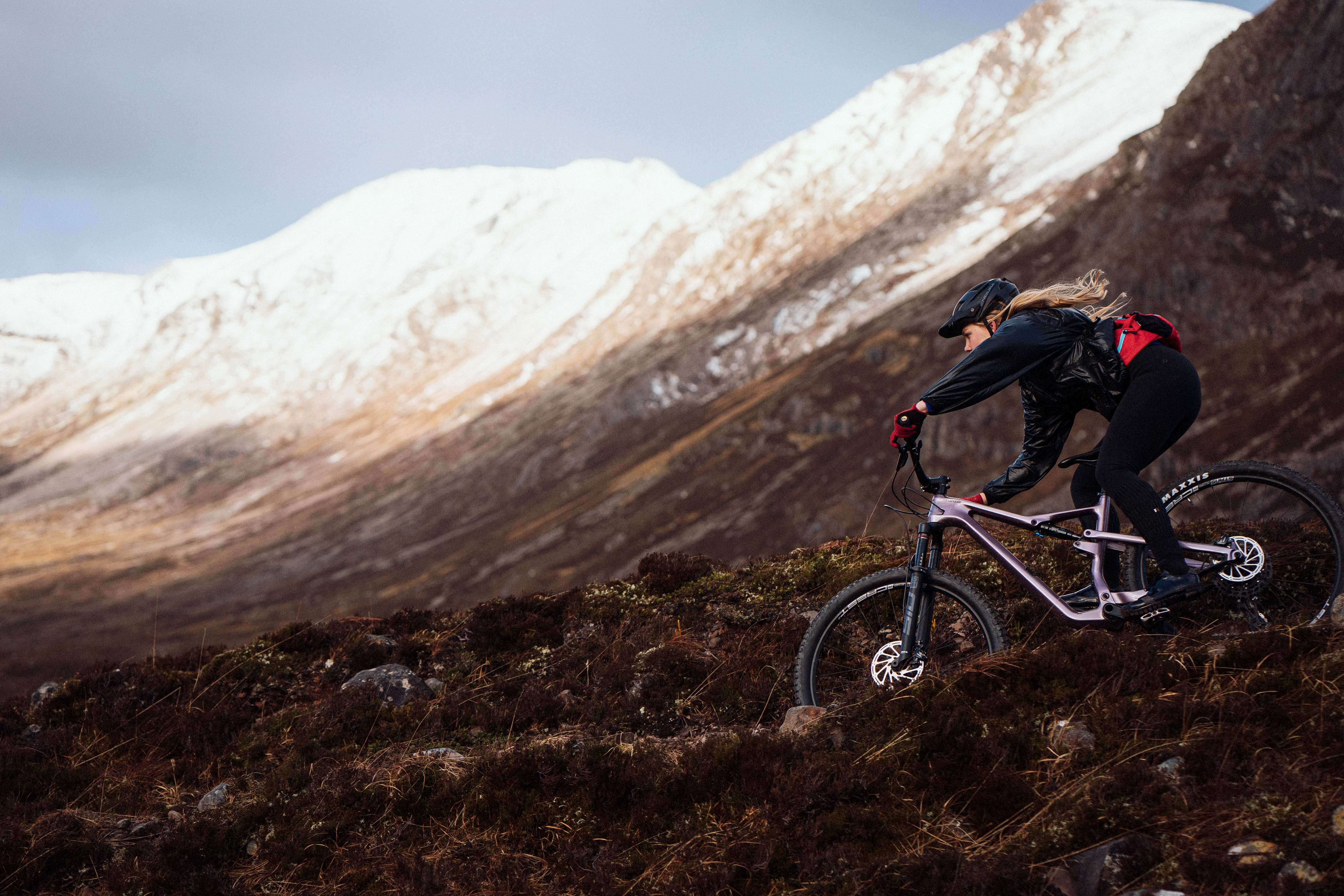 Frau fährt Cannondale-Mountainbike bergab in schneebedeckter Berglandschaft, geeignet für Offroad-Abenteuer.
