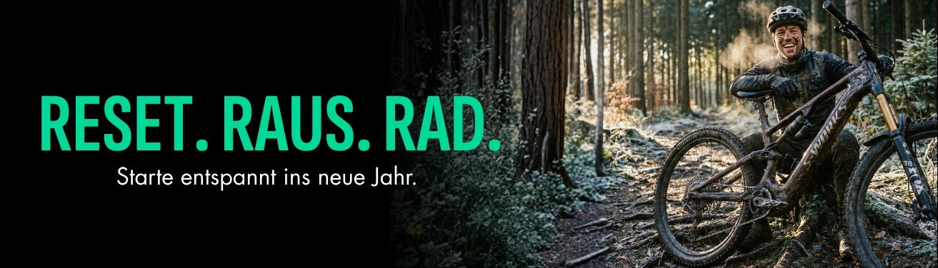 Mountainbiker sitzt lächelnd auf Waldboden mit einem verschmutzten Fahrrad, daneben Text: "RESET. RAUS. RAD."