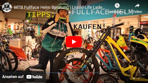 Mann in einem Fahrradladen, trägt einen Fahrradhelm, steht neben einem Mountainbike. Reichlich Fahrräder im Hintergrund.