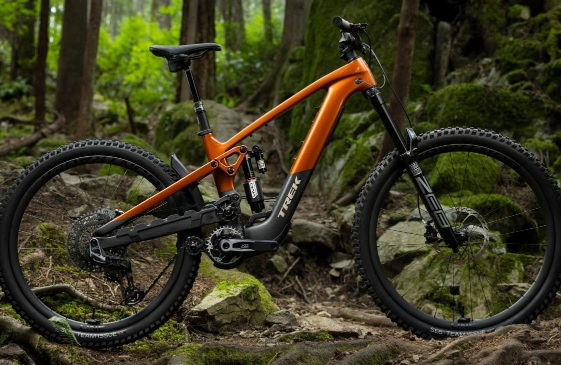 Orangefarbenes Trek-Mountainbike im Wald, ideal für anspruchsvolle Trails. Modellname auf Bild nicht ersichtlich.