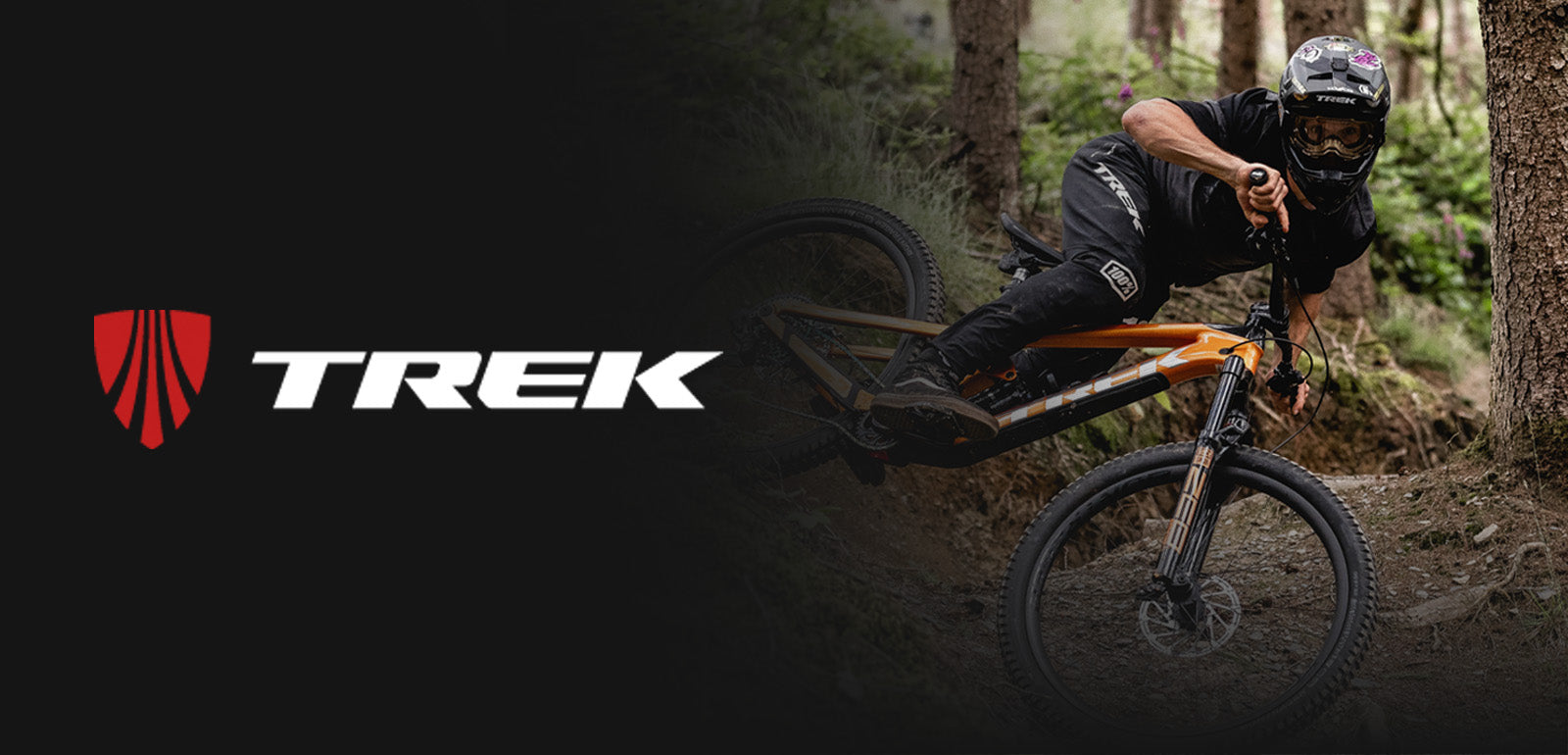 Mountainbiker auf orangefarbenem Trek-Fahrrad von der Seite, mitten im Wald auf schmalem Trail.