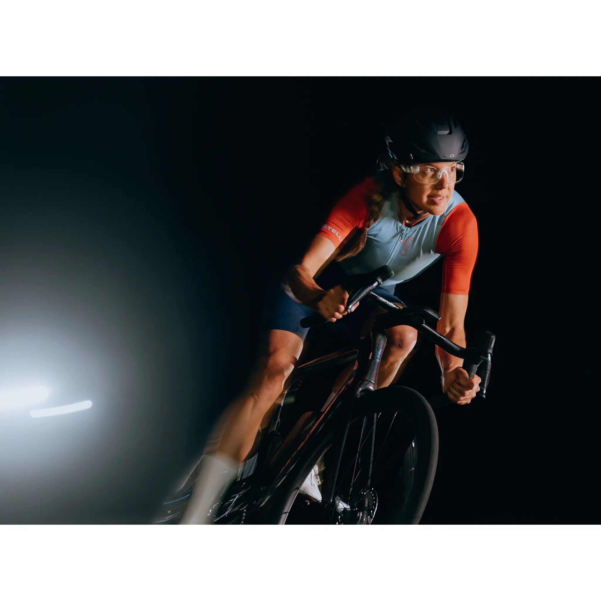 Cervelo Radfahrer in sportlicher Kleidung auf Rennrad bei Nachtfahrt, trägt Helm und Brille, Hintergrund dunkel.