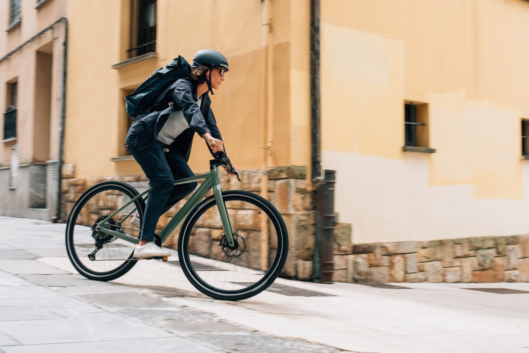 Person auf Orbea E-Bike fährt in städtischer Umgebung, trägt Helm und Rucksack. Ideal für Pendler oder Freizeitfahrer.