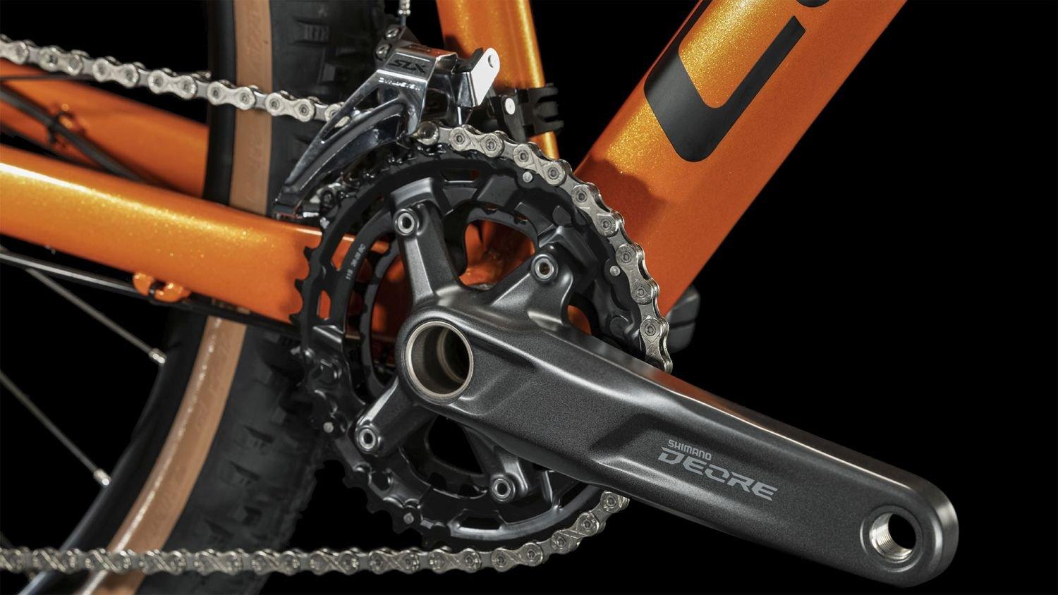 Nahaufnahme eines orangefarbenen Fahrrads mit Shimano Deore Kurbelgarnitur und Kette. Ideal für sportliche Radfahrer.