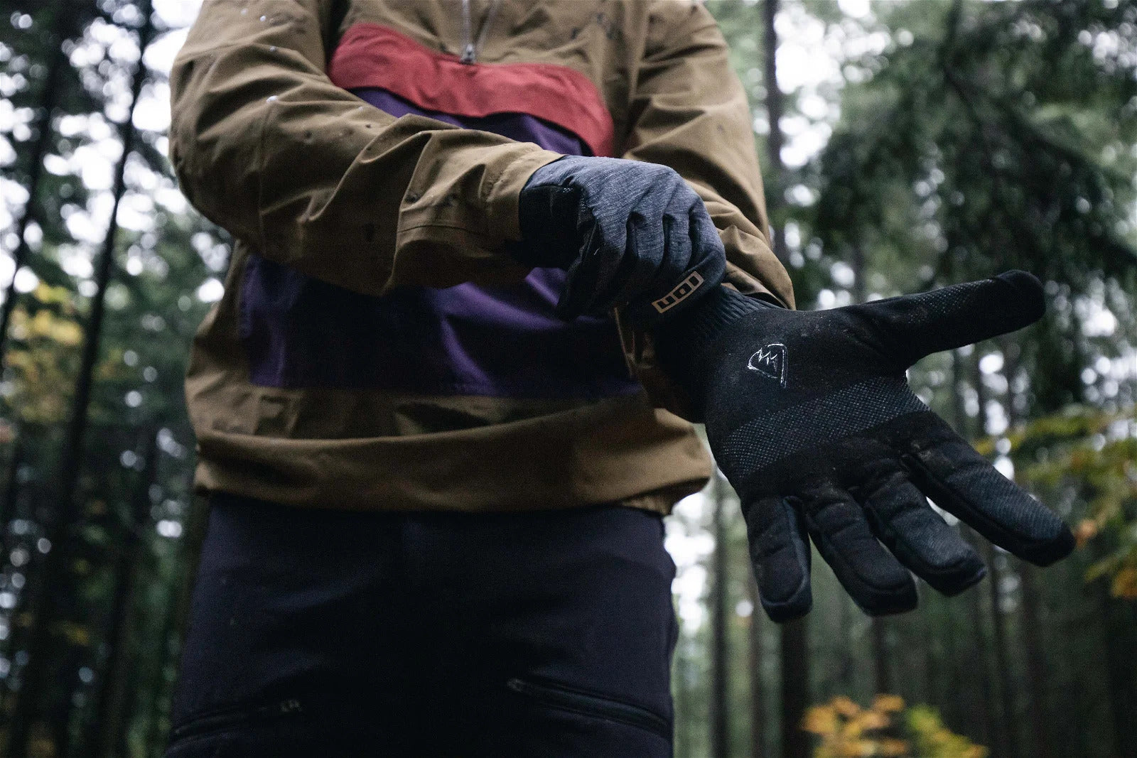 Person in Outdoor-Jacke zieht sich ION-Handschuh an, ideal für Aktivitäten bei Wind und Wetter im Wald.