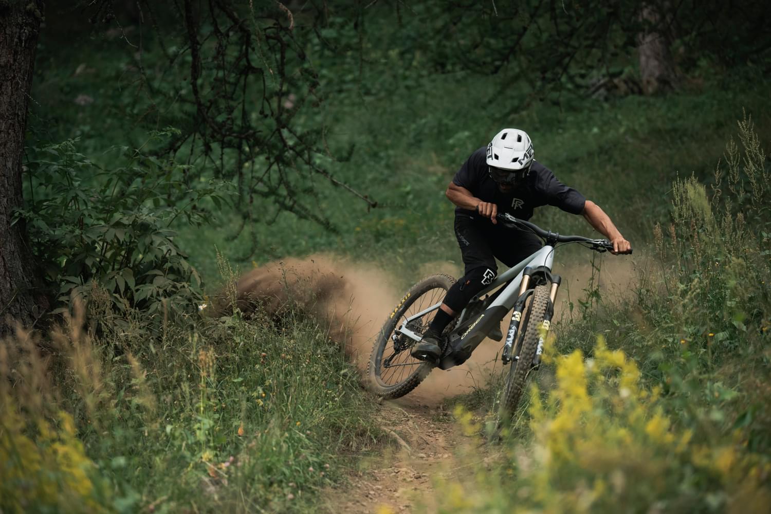 Mountainbiker fährt in schwarzer Ausrüstung schnell durch Waldweg, spritzt Staub auf. Ideal für Downhill-Enthusiasten.