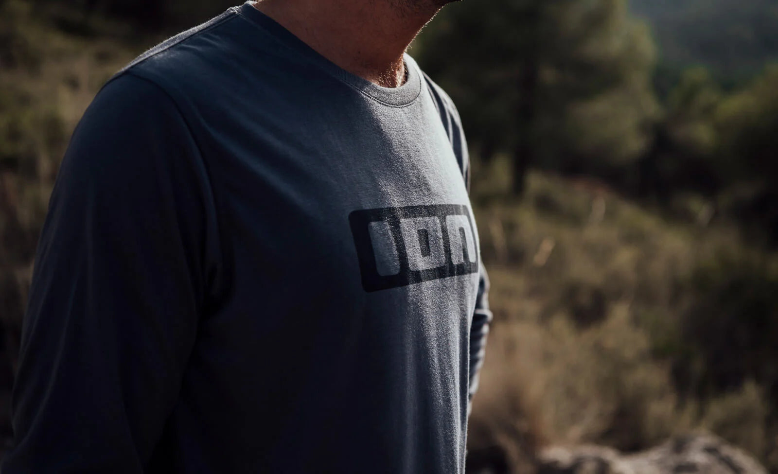 Person trägt dunkelgraues Langarmshirt von ION mit Logo, geeignet für Outdoor-Aktivitäten.