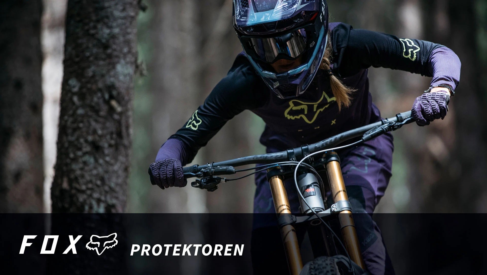 Fahrerin mit FOX Protektoren und Helm auf Mountainbike im Wald, Fokus auf Schutzbekleidung und Action.