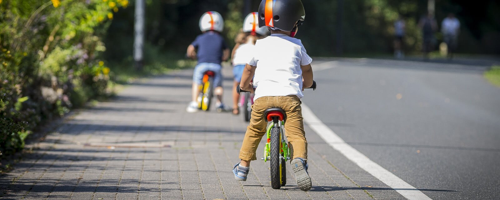 Kinder fahren auf Laufrädern auf einem Weg. Sie tragen Helme. Ideal für den Einsatz im Freien. Puky Laufräder.