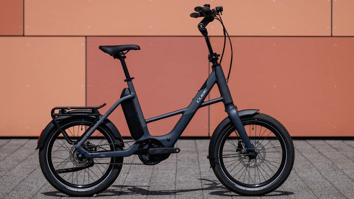 Schwarzes Cube COMPACT HYBRID DELUXE 540 mit tiefem Einstieg, geeignet für Stadtverkehr, vor orangefarbener Wand fotografiert.