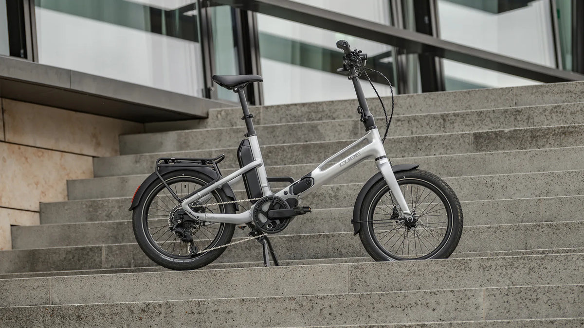 Silbernes Cube Falt-E-Bike FOLD HYBRID 540 auf Treppe, ideal für urbane Pendler, kompakt und praktisch für kurze Wege.