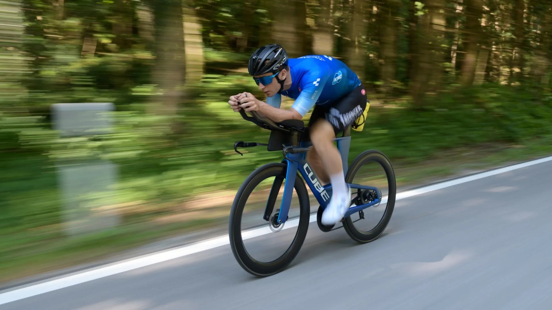 Radfahrer auf Cube Aerium in Aktion, schneller Sprint auf einer Straße durch bewaldete Landschaft.