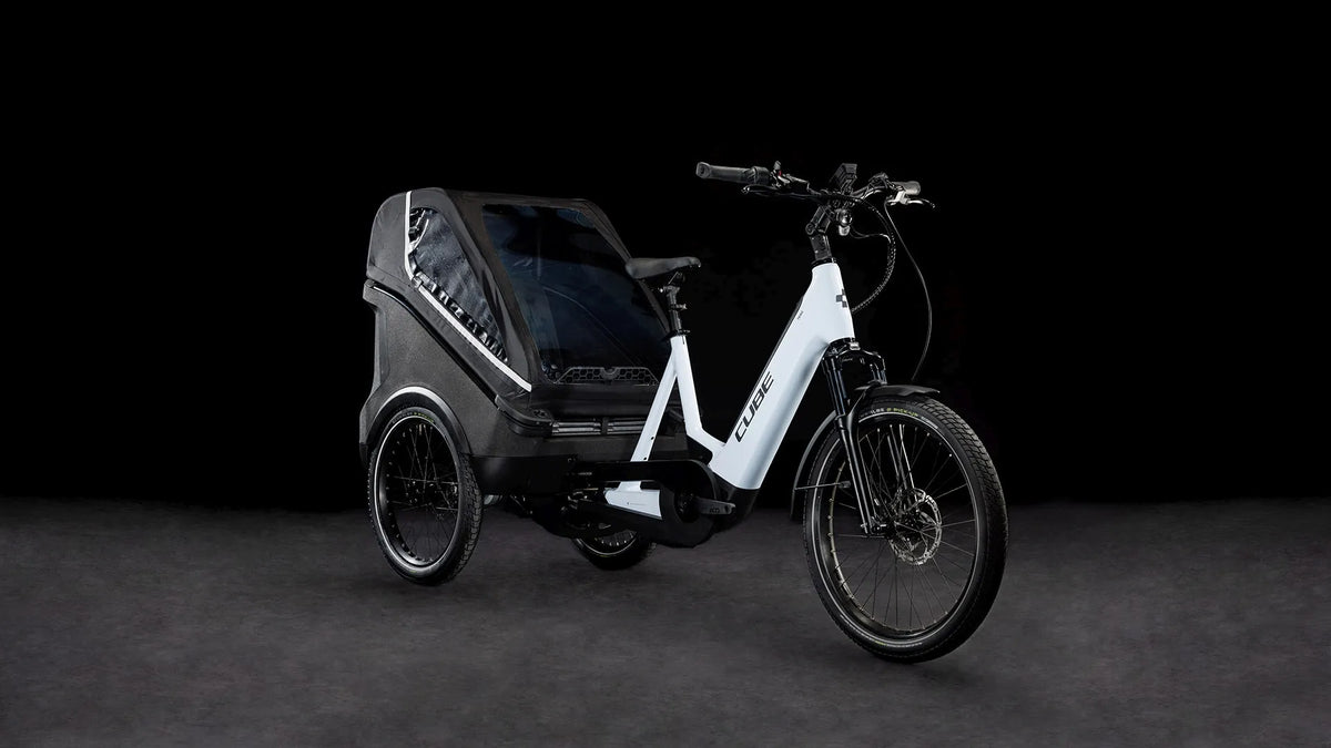 Lasten-E-Bike CUBE TRIKE FAMILY HYBRID 750 mit Anhänger für Transport oder Familienausflüge, weißes Design, geeignet für urbane Mobilität.